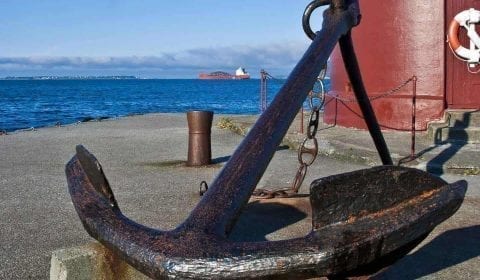 Massive anchor on a small pier in front of a red lighthouse in the center of Ålesund