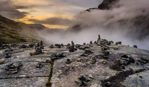 Utsikt over varder på toppen av Trollstigen og tåke som henger i dalen