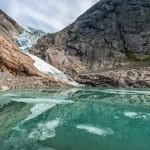 Klarer blauer Gletschersee vor dem Briksdaler Gletscher, umgeben von Bergen