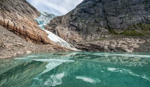 Klarer blauer Gletschersee vor dem Briksdaler Gletscher, umgeben von Bergen