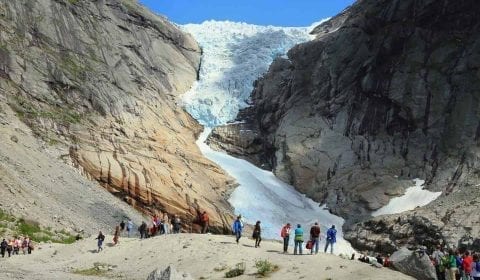 Turisti visitano il ghiacciaio di Briksdal, un braccio di ghiacciaio sulle montagne alte sotto un cielo limpido