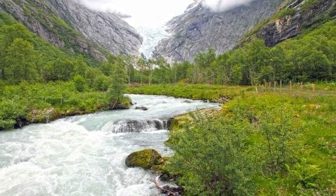 El agua fluye desde el glaciar Briksdal a través del valle verde rodeado de altas montañas