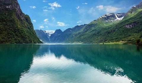 Turquoise water in lake Oldevatnet, surrounded by green mountains on a clear day, Melkevoll Glacier on the mountains in the background