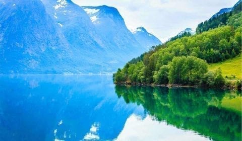 Montañas altas cubiertas de árboles verdes que rodean un lago de montaña