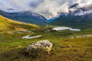 Fjellvei gjennom Reinheimen Nasjonalpark, liten innsjø og fjelltopper i skyene