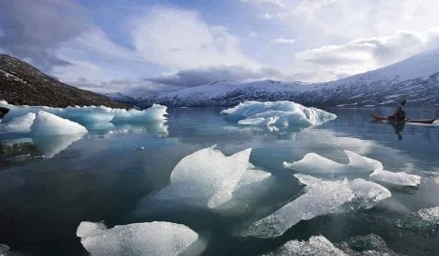 Kayakiste sur un lac glaciaire, blocs de glace flottant sur l'eau