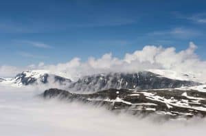 View from Mount Dalsnibba over Lake Djupvatn covered under the clouds, mountain peaks with snow stick out above the clouds