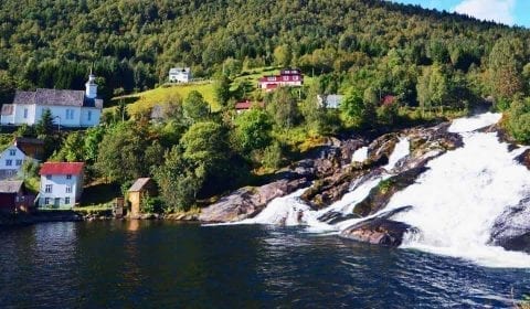 Hellesylt waterfall streaming from the mountain in the fjord, houses and church on the mountainside