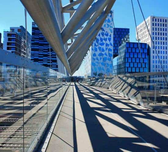 El acróbata, un puente peatonal, en el barrio del Código de Barras en Oslo, edificios modernos en el fondo