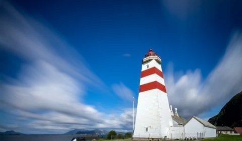 Der rot-weiße Leuchtturm von Alnes auf der Insel Godoy unter einem blauen Himmel mit ein paar weichen Wolken