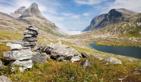 Ometto di pietra accanto a un prato verde a un piccolo lago nelle montagne alte vicino alla Strada dei Troll in Norvegia