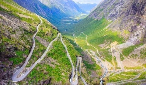 Utsikt over Trollstigen i en grønn dal omringet av høye fjell