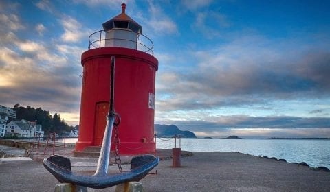 Liten brygge med et anker og et rødt fyrtårn ved solnedgang i Ålesund, Norge