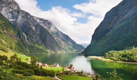 Green fjord surrounded by high mountains, farms on the shore