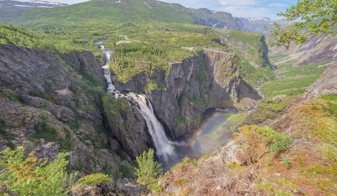 Arc-en-ciel dans les gouttes de l'éblouissante cascade Voringsfossen dans les montagnes vertes