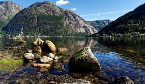 Felsen im klaren Wasser eines Fjords vor Eidfjord unter einem klaren blauen Himmel