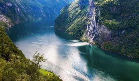 Fossen de Syv Søstre strømmer nedover en bratt fjellside mot den turkise Geirangerfjorden