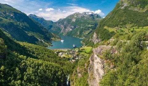 Utrolig utsikt fra Flydalsjuvet, grønne fjell omringer Geirangerfjorden under en blå himmel, to skip besøker Geiranger, Norge