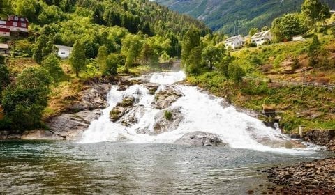 Cascata scorre giù per le montagne verdi, case di legno a Hellesylt, Norvegia