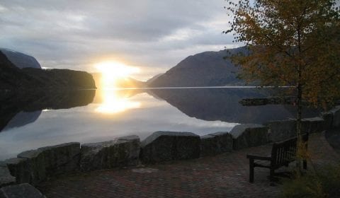 Panoramautsikt mot en solnedgang over en rolig innsjø, Hornindalsvatnet, omringet av fjell som gjenspeiles i vannet