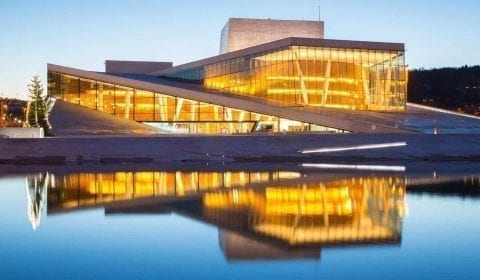 The Oslo Opera House with lights on, reflecting in the water