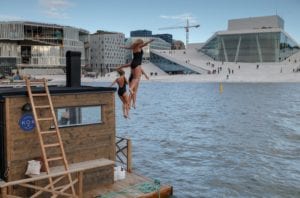 Three women jump from a floating sauna into the Oslo Fjord across from the Opera House