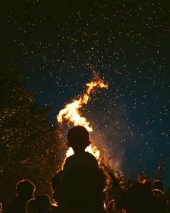 A silhouette of a child on their parent's shoulders watching a midsummer bonfire