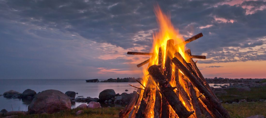 a bonfire next to the ocean during midsummer