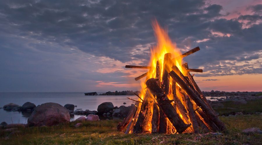 a bonfire next to the ocean during midsummer
