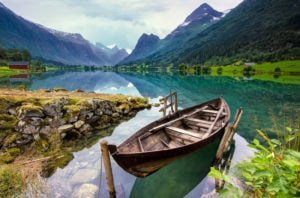 a wooden boat is docked on the side of the beautiful Loen lake in Norway.