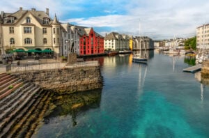 Veduta di Brosundet Ålesund, Norvegia, con edifici colorati lungo l'acqua, barche ormeggiate nel porto e una statua in primo piano.